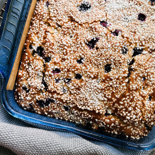 A close-up of the Cardamom Pearl Tea Cake (Kit) in a glass dish, topped with Swedish pearl sugar and dark berries, resting on a woven cloth.