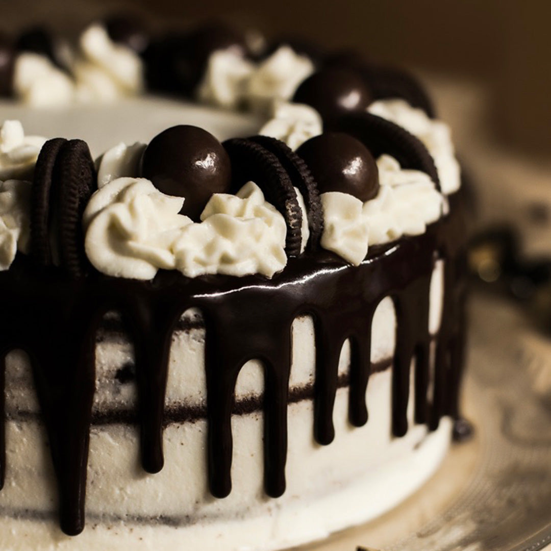 Chocolate cake with white frosting, chocolate drizzle, and Oreo cookies on a blurred background