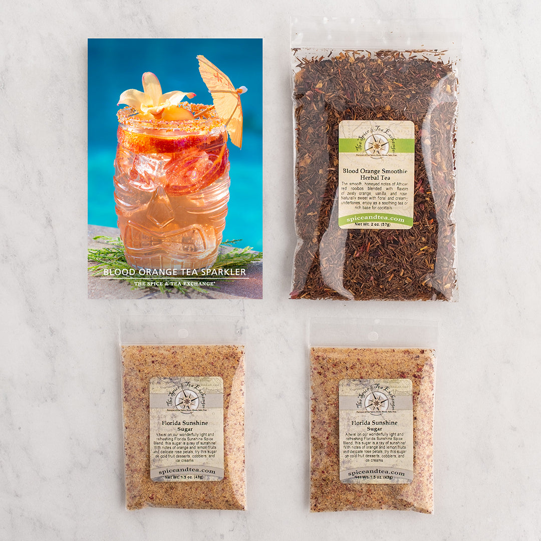 Three tea & sugar products arranged on a light marble surface and a branded recipe card reading Blood Orange Tea Sparkler.