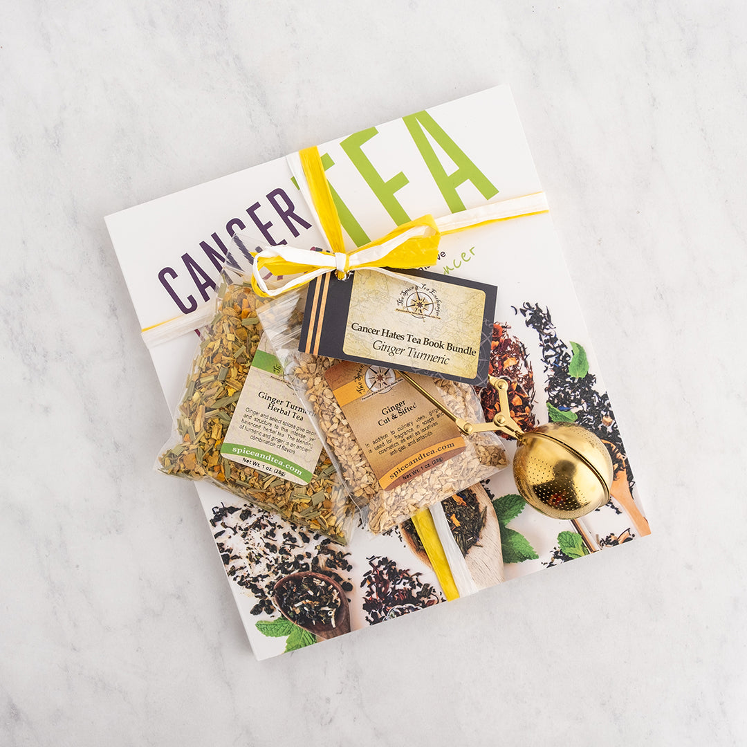 A tea gift set arranged on a white marble surface, featuring a white book, Ginger Turmeric Herbal Tea, Ginger - Cut & Sifted, a yellow ribbon, a small gold scissors infuser, and a tag reading 'Cancer Home Tea Book Bundle Ginger Turmeric.'