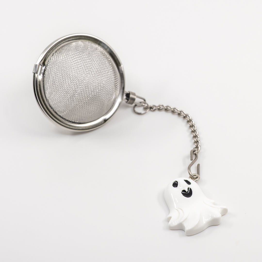 Tea ball with mesh filter and ghost charm on a white background
