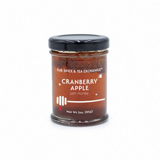 The Cranberry Apple Jam Honey Jar is a 3 oz (85g) glass jar from The Spice & Tea Exchange, featuring a black lid and white-lettered label. Made with raw natural honey, it offers a perfect blend of sweet and tart flavors.