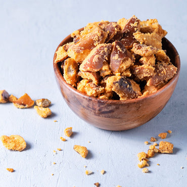 Wooden bowl filled with crumbly snack on a light blue background