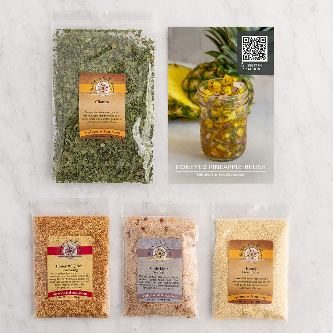 Four packaged food products arranged on a light marble surface: next to a recipe card for Honeyed Pineapple Relish.