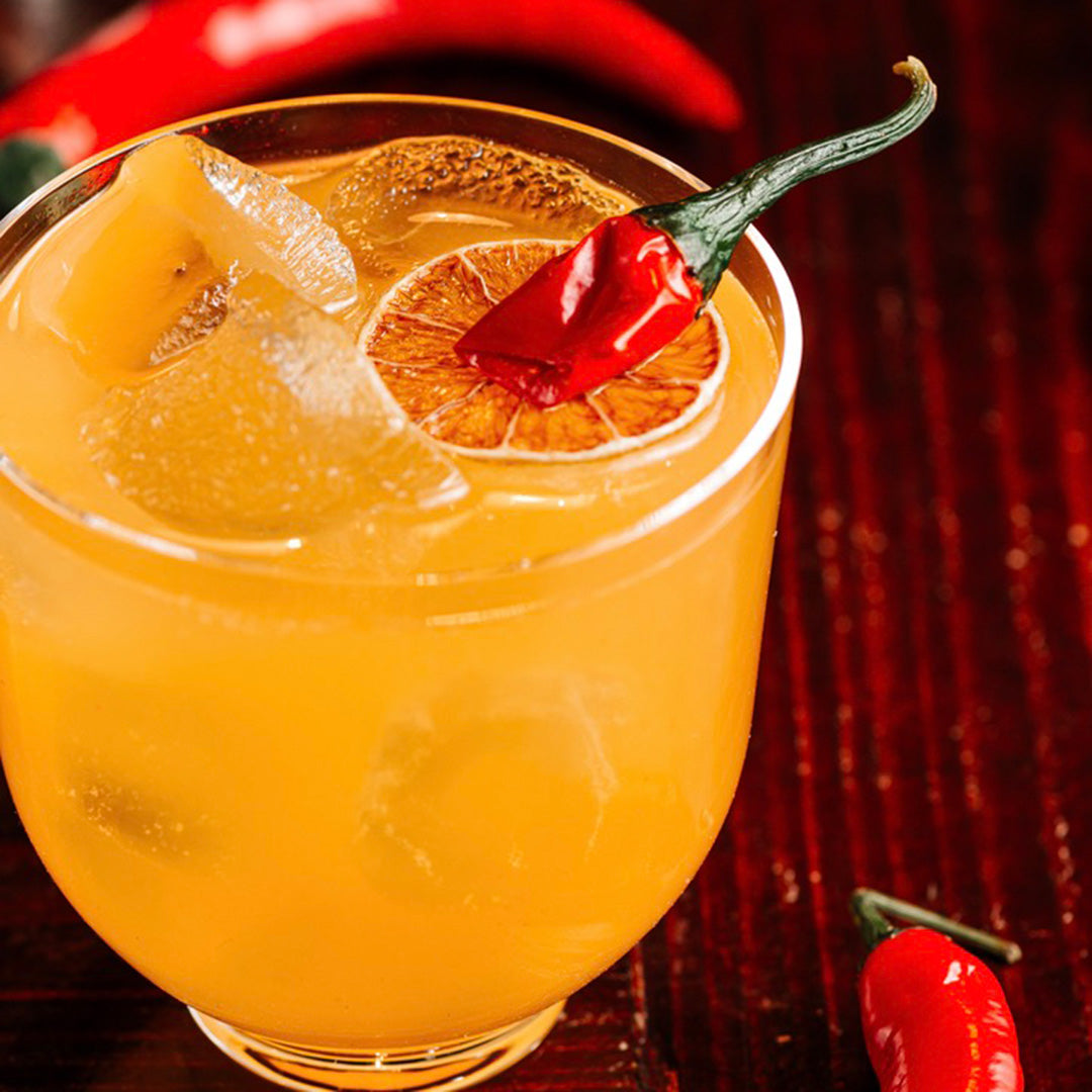 Orange cocktail with a chili pepper garnish on a dark background