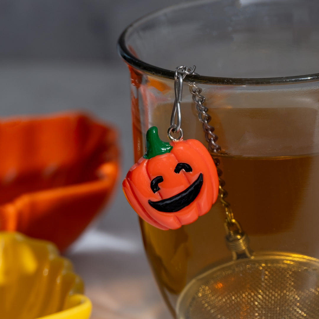 Pumpkin-shaped charm and tea ball infuser on a glass with a blurred background.
