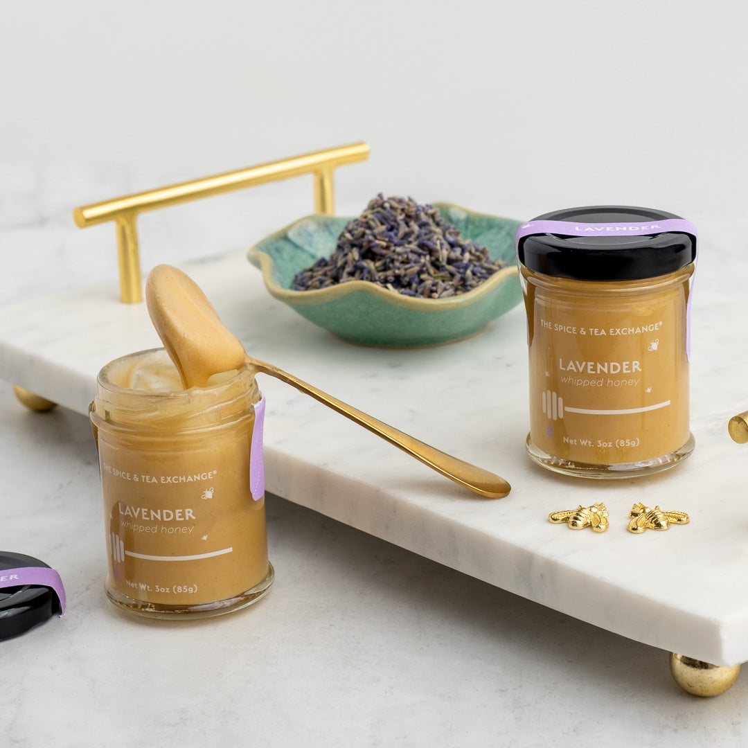 Lavender Whipped Honey Jars on white marble platter with bent honey spoon and next to a bowl of lavender