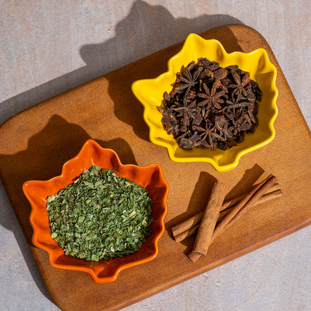 Spices including star anise and cinnamon sticks on a wooden board with two bowls.