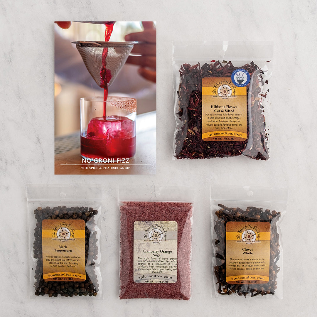 A flat-lay of No'groni Fizz recipe card and four individual bags of loose-leaf blends: Hibiscus Flower, Black Peppercorns, Cranberry Orange Sugar, and Cloves Whole.