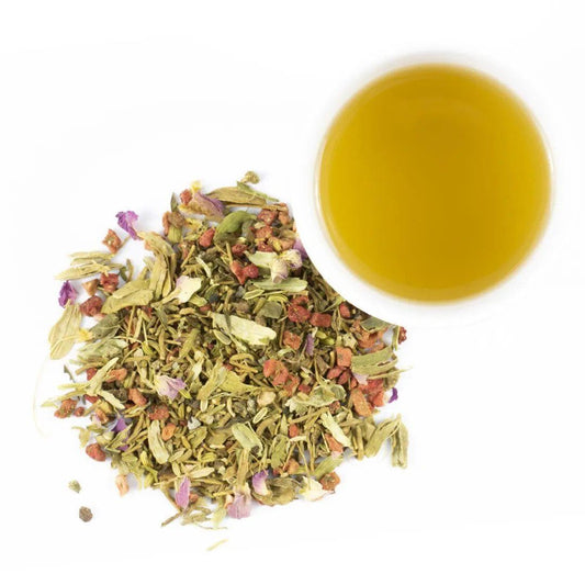 A cup of Beauty Rest Herbal Tea sits beside a loose pile of relaxing botanicals and flowers, including valerian root, on a white background.