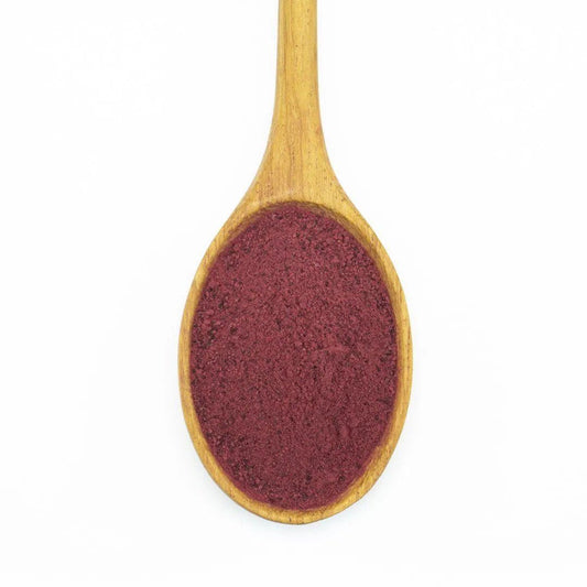 A wooden spoon holds Organic Beet Root Powder—finely ground and dark red, renowned for its nutritional benefits—photographed on a white background.