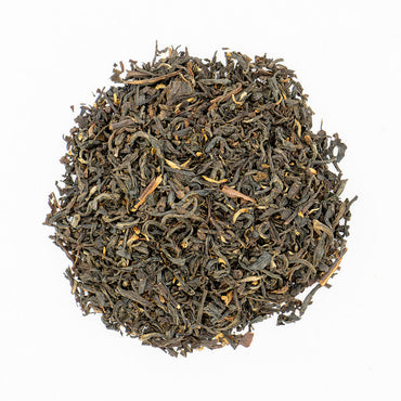 A circular pile of loose-leaf tea leaves, predominantly dark brown and black with lighter tan and yellowish-brown accents, photographed from directly above on a solid white background.