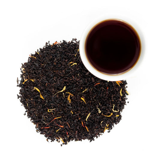 A cup of Peach On The Beach Tea rests atop a pile of black tea leaves, offering a fruity and soothing moment to unwind.
