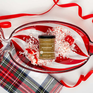 Jar of peppermint honey on a candy cane-themed platter with red ribbon and plaid fabric.