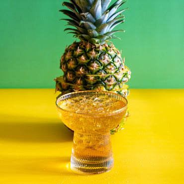 Pineapple Paradise Green Tea iced in a glass next to a sliced pineapple