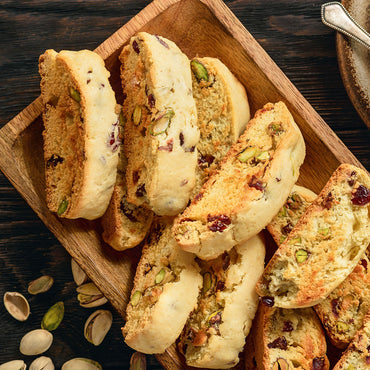 Biscotti cookies filled with pistachios and cranberries, arranged on a wooden serving tray with a few pistachios scattered on a dark wooden table.