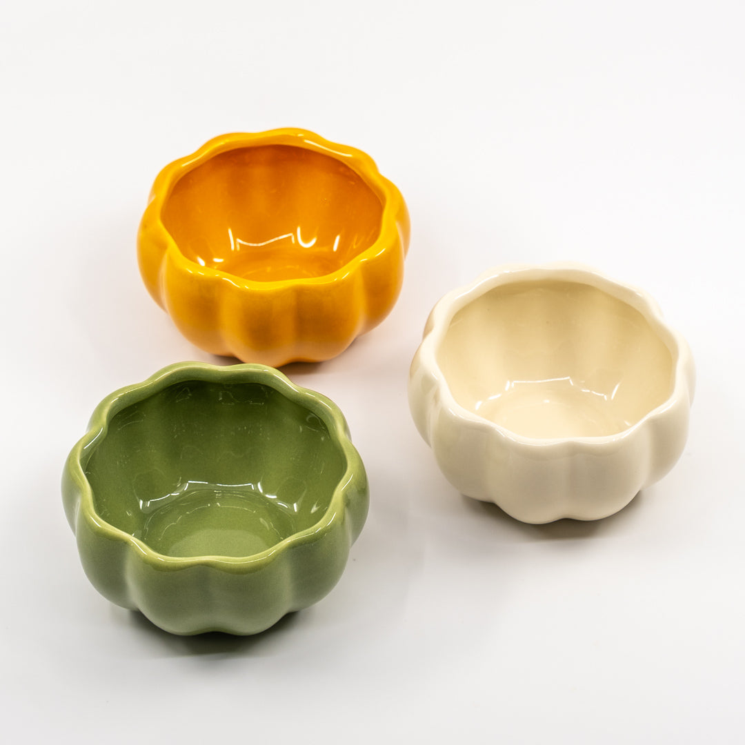 Three pumpkin ceramic bowls in orange, green, and beige on a white background