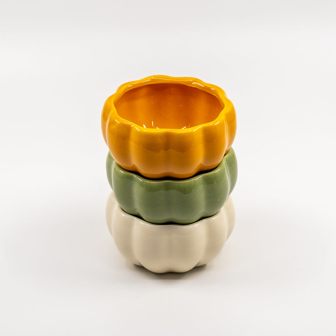 Stack of three ceramic pumpkin bowls in orange, green, and beige on a white background