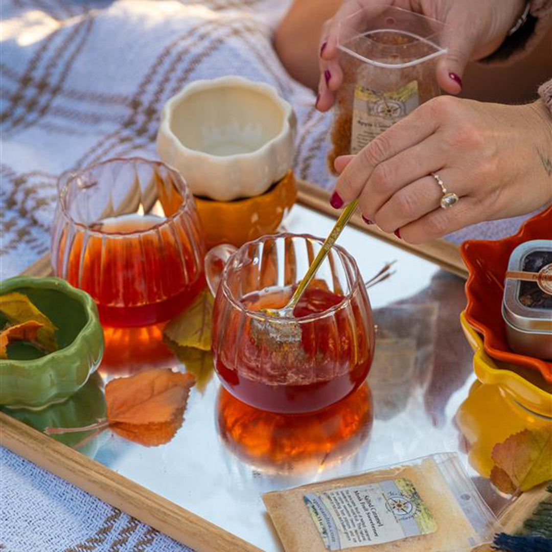 Person preparing a cup of tea with a teabag on a table with autumn leaves.