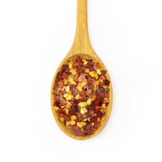 A wooden spoon holds Crushed Red Pepper Flake, made from dried chile peppers like cayenne, displayed on a white background.