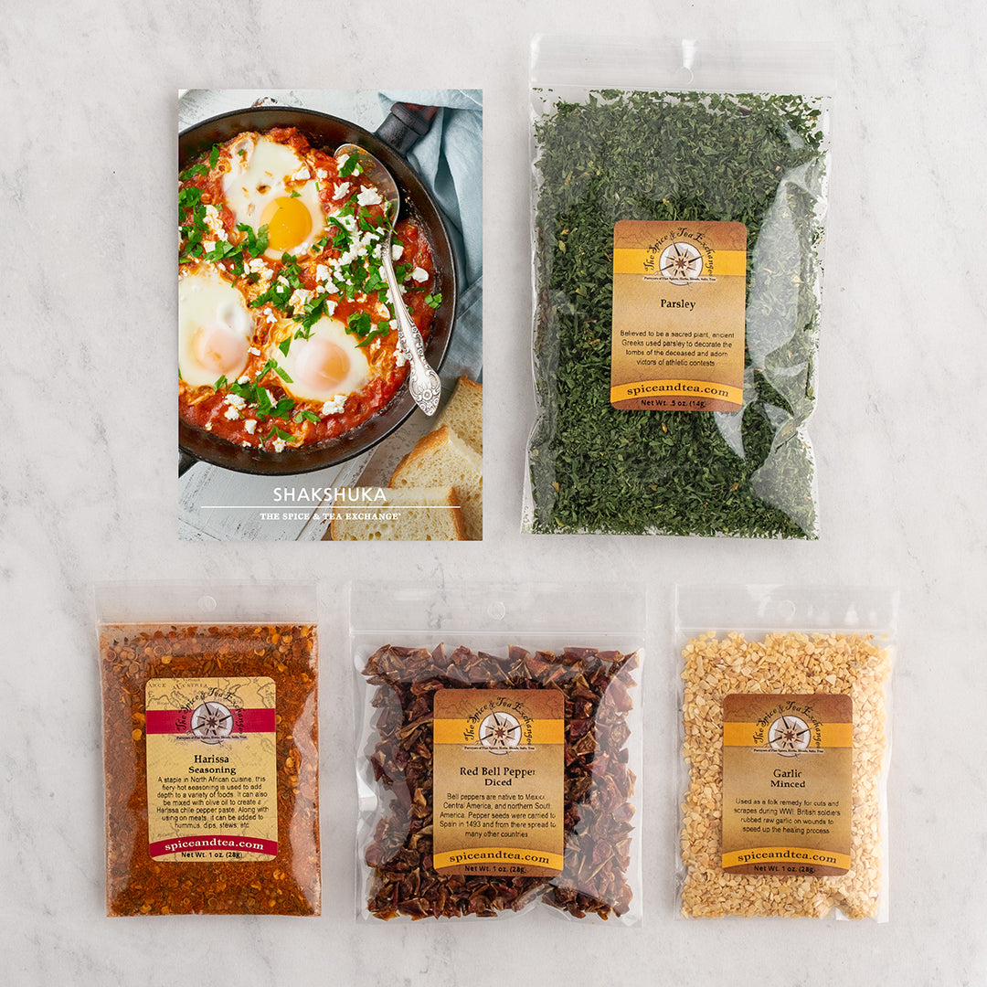 Shakshuka recipe card on tile background next to four bags of spices.