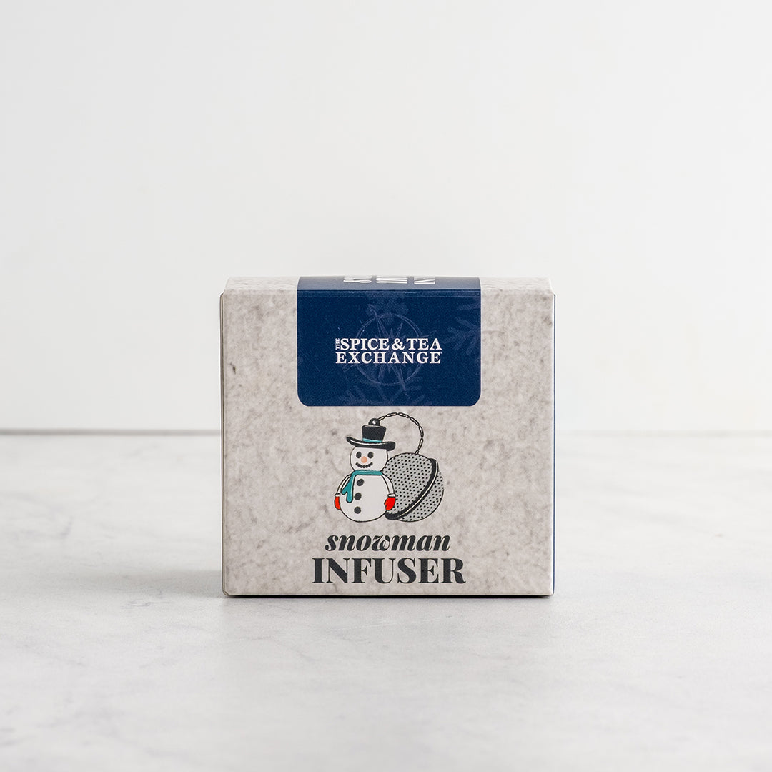 A square product box for a 'Snowman infuser' by 'THE SPICE & TEA EXCHANGE' on a light gray marble surface against a white background.