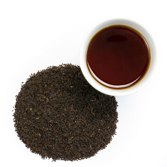 A white cup of Southern Iced Tea sits beside a large pile of loose black tea leaves, highlighting their traditional flavor on a white background.