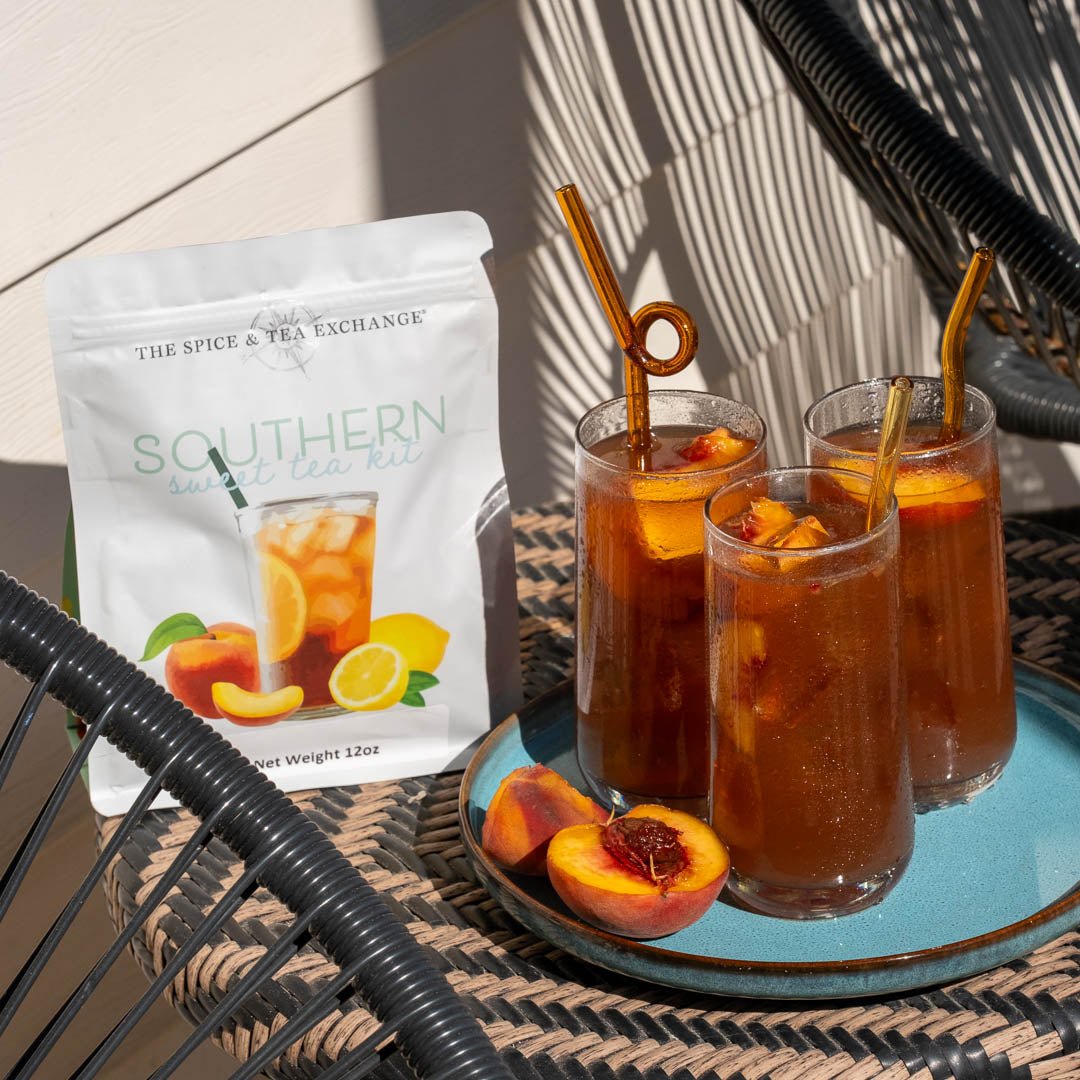 Southern Sweet Tea Kit on patio chair next to three tall glasses of iced cold southern sweet tea and peach slices
