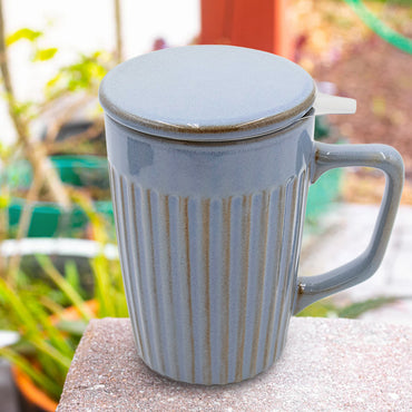 Blue ceramic mug with a lid on a stone surface with a garden background