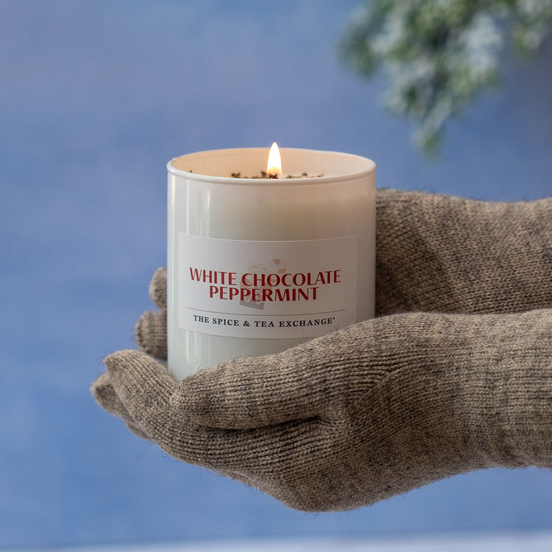 Hand holding a 'White Chocolate Peppermint' candle against a blue background