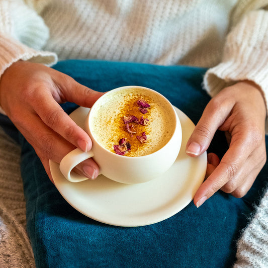Golden Milk in White Mug with Spices Sprinkled on Top and Hands Holding Mug