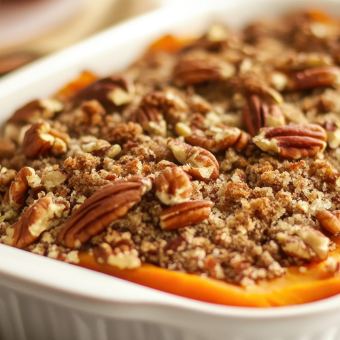 A close-up of a baked sweet potato casserole topped with a crumbly pecan and brown sugar streusel in a white baking dish.