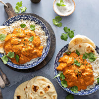 Enjoy two bowls of Butter Chicken (Kit) curry over rice, garnished with cilantro and served with naan bread. Perfect for creating a delicious meal using your favorite seasoning kit.