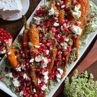 Roasted Carrots (Kit) features roasted carrots with crumbled feta, fresh herbs, and pomegranate seeds on creamy Green Goddess dip, served on a rectangular white platter.