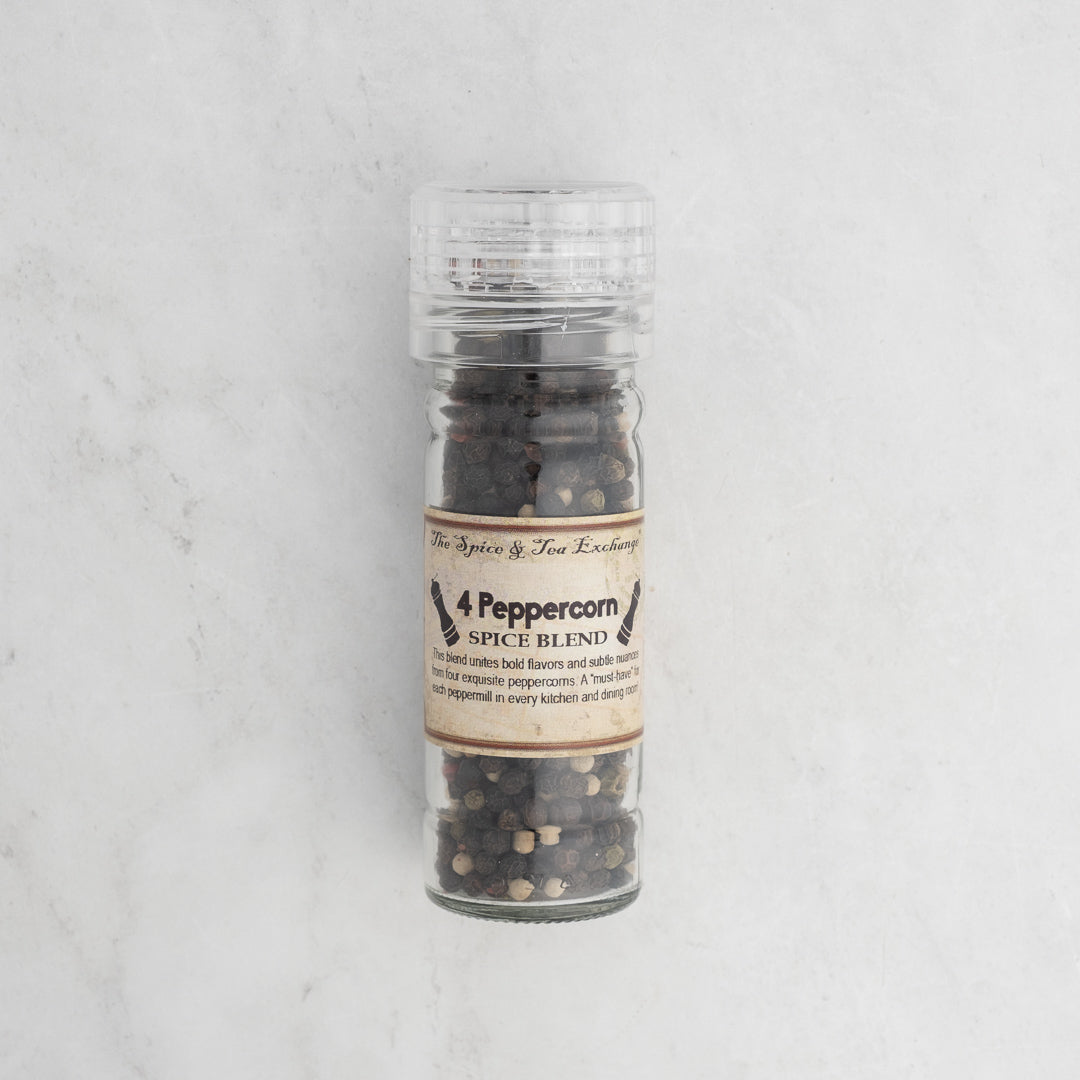 The 4 Peppercorn Spice Blend in a clear glass peppermill features a vibrant mix of whole black, white, and pink peppercorns—an eye-catching addition to any kitchen countertop.