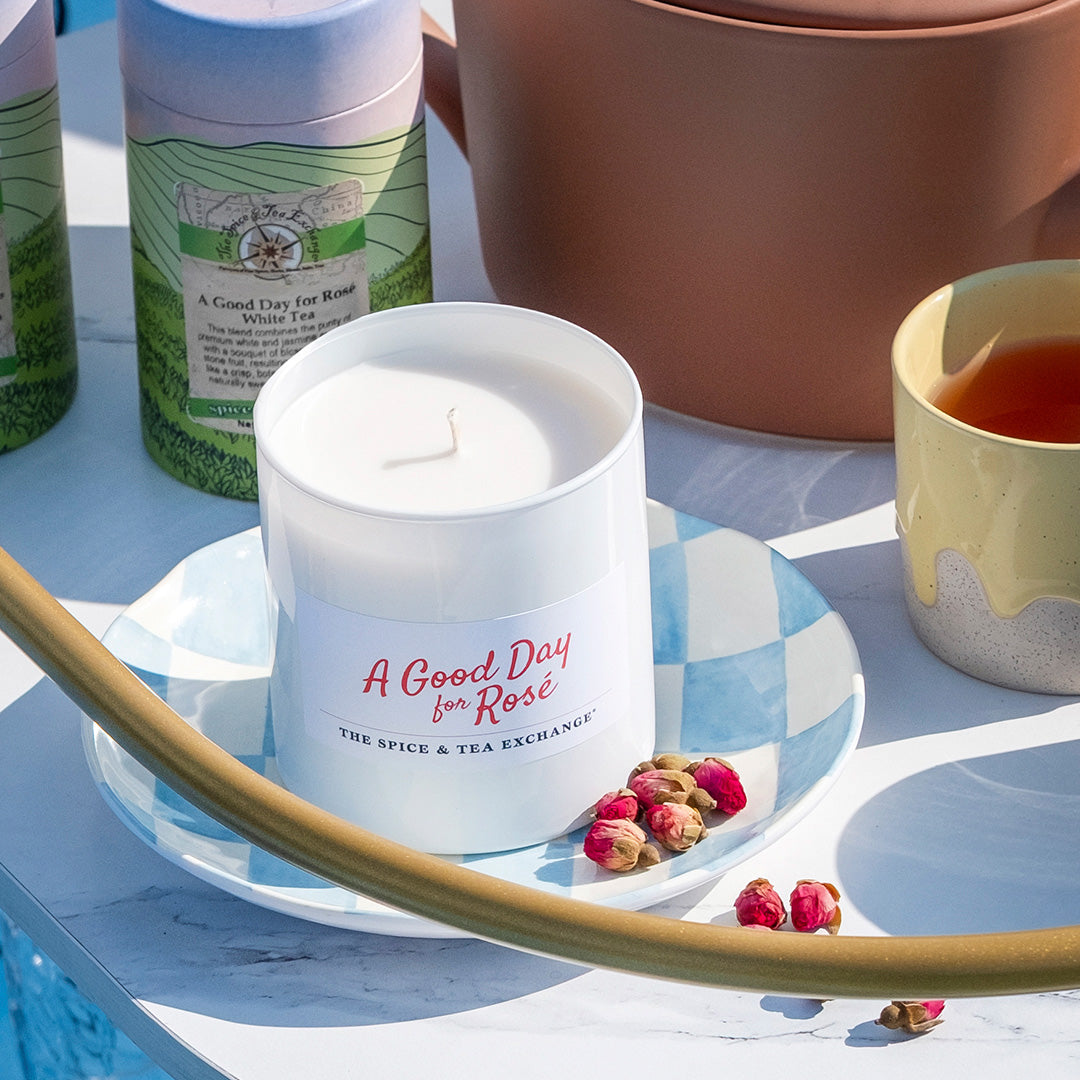 Candle labeled 'A Good Day for Rosé' on a decorative plate with tea and tea packaging in the background.