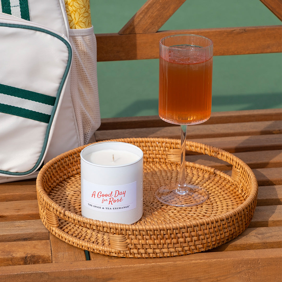 Candle and glass of A Good Day for Rose tea on a woven tray with a bag in the background