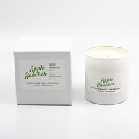 A candle in a white glass jar next to its white packaging box, both featuring the 'Apple Rancher' brand logo in green script on a clean white background.