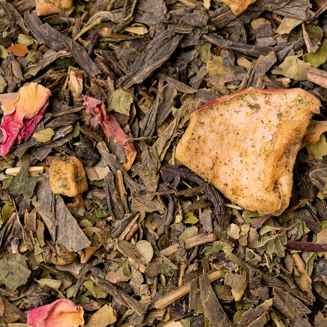 Close-up of loose-leaf herbal tea with dried leaves, tea bags, and a dried fruit piece on a white background.