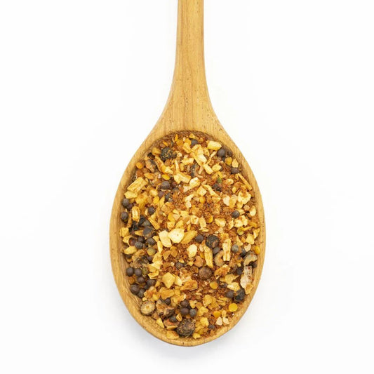 A wooden spoon filled with Backwoods Hickory Rub Seasoning—a colorful blend of dried spices like crushed red pepper, dried garlic, and seeds—makes a rustic grilling rub or seasoning, displayed against a white background.