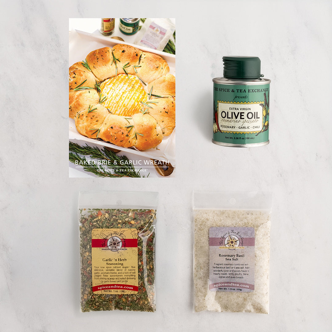 A flat-lay product arrangement on a light marble surface featuring a Baked Brie and Garlic Wreath recipe card. Featuring 3 products.