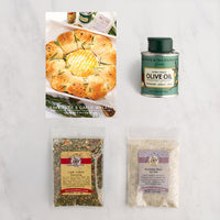 A flat-lay product arrangement on a light marble surface featuring a Baked Brie and Garlic Wreath recipe card. Featuring 3 products.