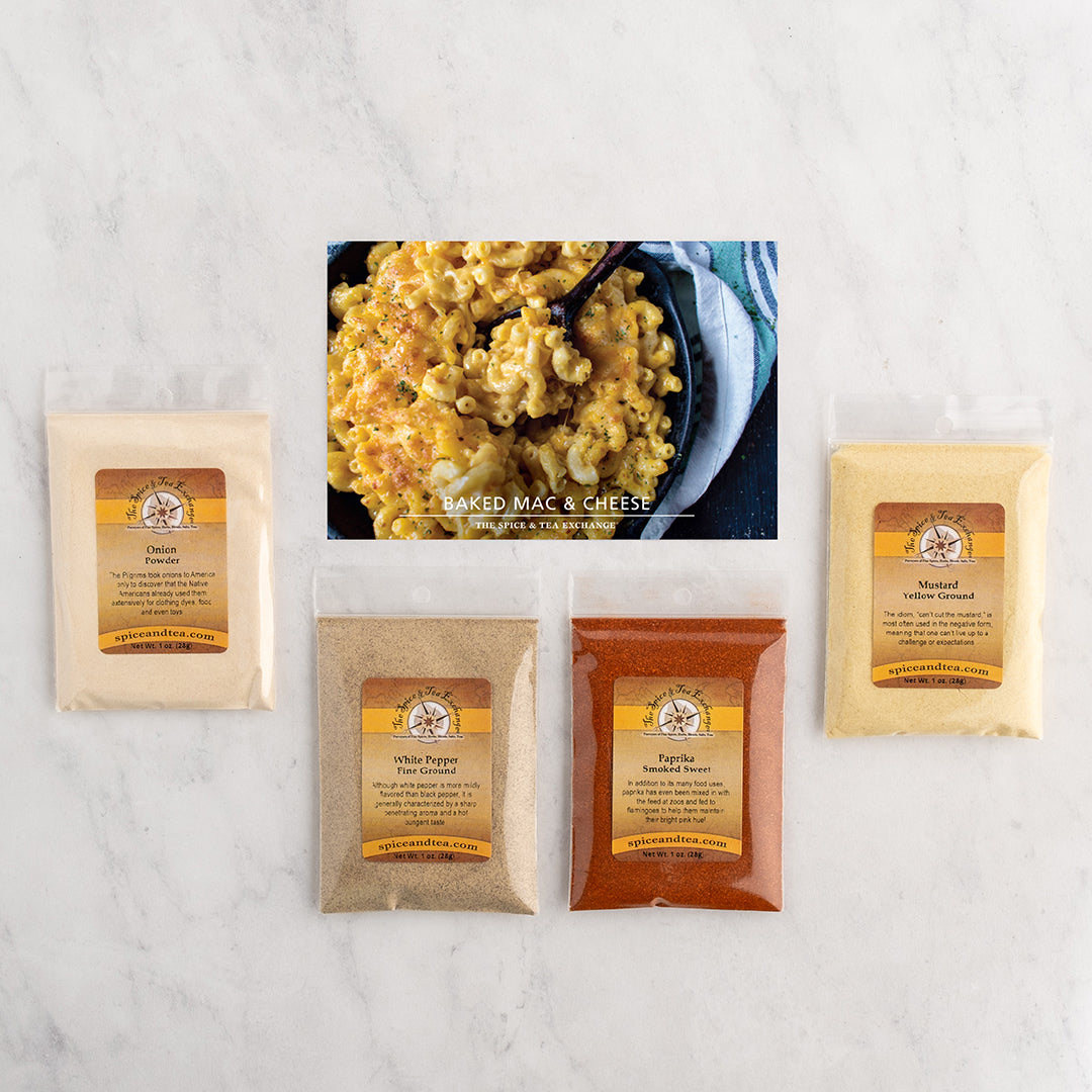Four seasoning/spice pouches arranged around a central printed recipe card showing baked mac and cheese.