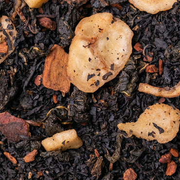 Close-up of loose-leaf tea with dark dried tea leaves mixed with pale beige dried fruit slices and small reddish-brown pieces.
