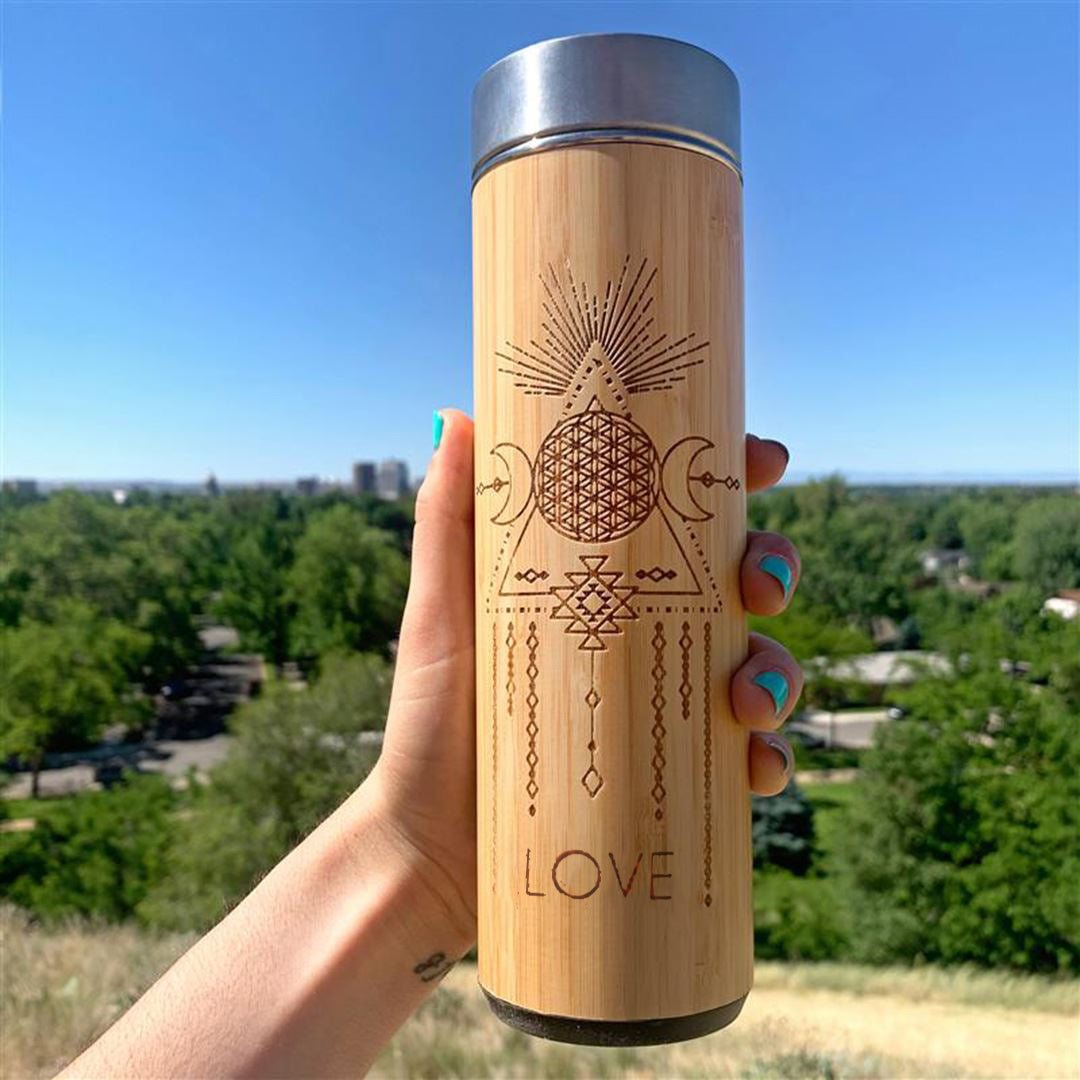 Wooden tumbler with geometric design and 'LOVE' text held against a scenic background