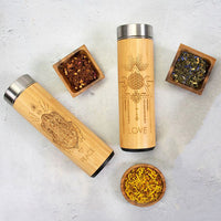 Two wooden thermos bottles with engraved designs on a light gray surface with small containers of dried herbs.