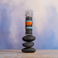 Black Lava sea salt grinder on stacked stones with a blurred background.