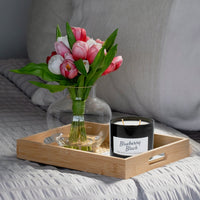 Bouquet of pink and white tulips in a clear vase on a wooden tray with a black candle labeled 'Blueberry Black' on a bed.
