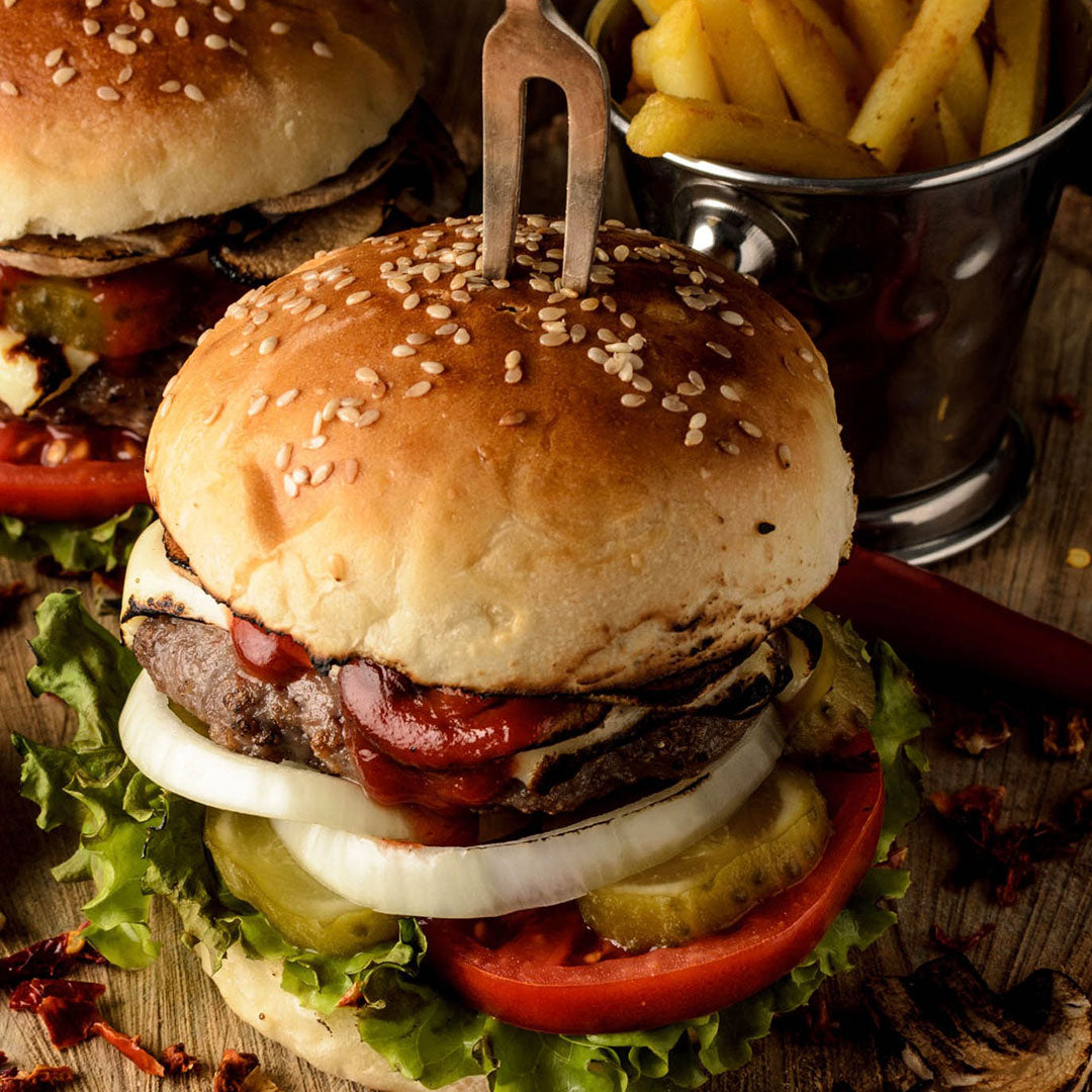 Burgers stacked with ketchup, cheese, onions, beef, pickles, tomatoes, lettuce, and served with fries