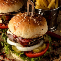 Burgers stacked with ketchup, cheese, onions, beef, pickles, tomatoes, lettuce, and served with fries